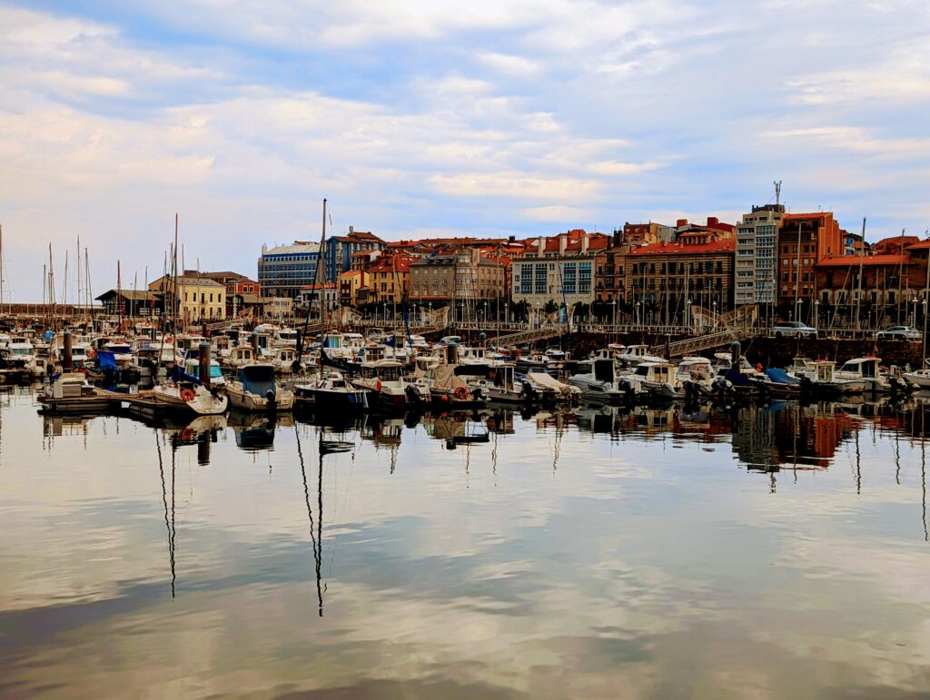 Gijon harbour with boats in the foreground, reflected in the water.