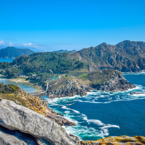 Scenic view of the coast of the Cies Islands, Vigo, featuring rocky cliffs and clear blue waters under a bright sky.