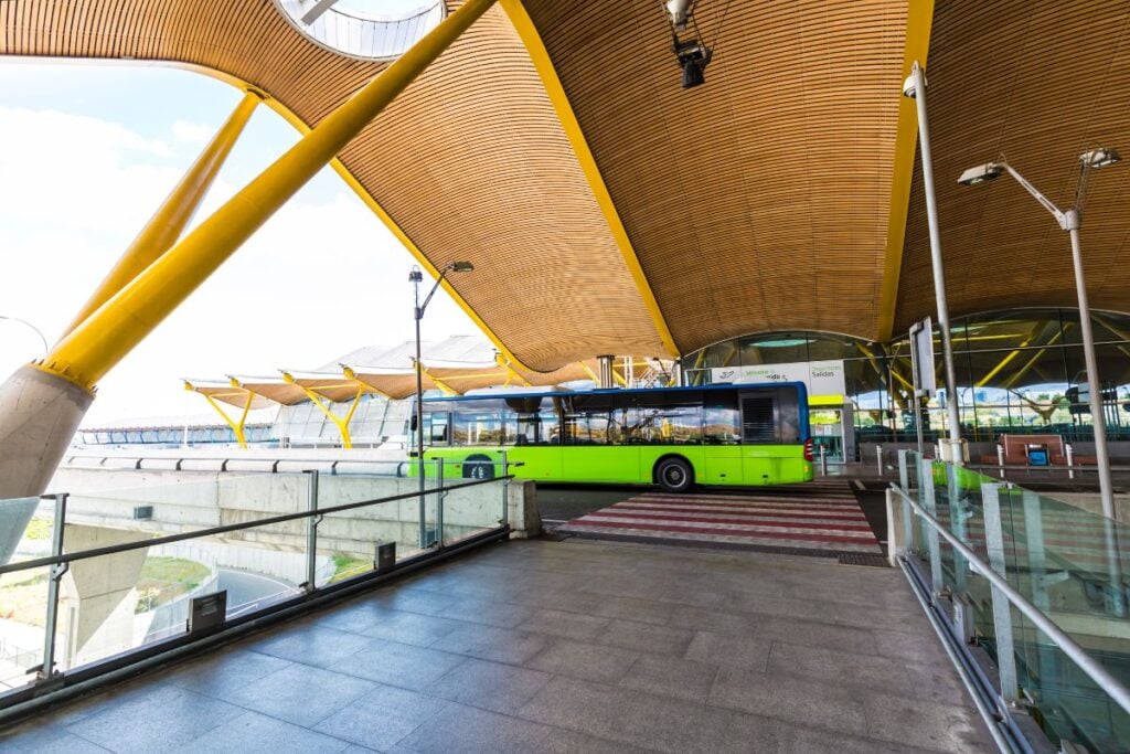A green bus is parked at the airport, prepared to take travelers to the centre of Madrid.