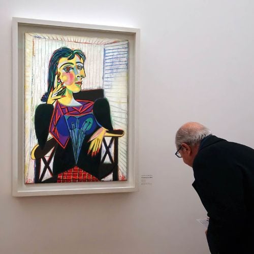 A man in a museum looking at a Picasso painting of a woman.