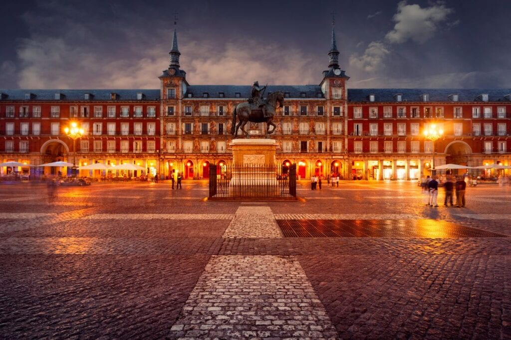 Plaza Mayor in Madrid illuminated at night with people enjoying the square.