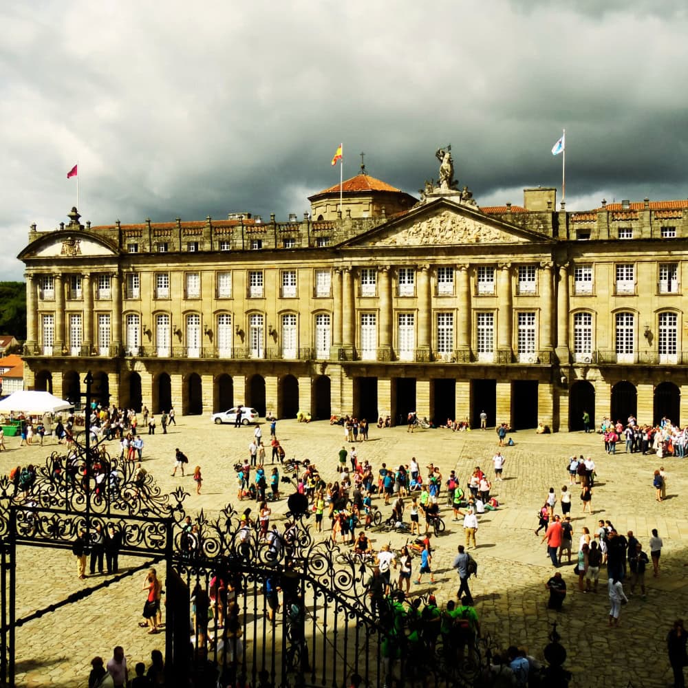 A large building in Santiago de Compostela, Spain, bustling with many people outside.