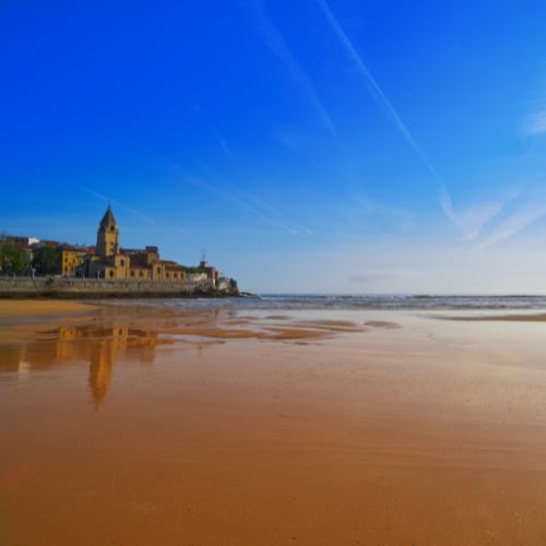 A scenic view of San Lorenzo beach in Gijon, featuring a church situated along the shoreline.