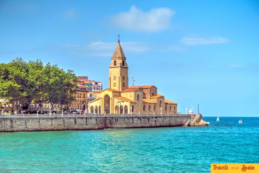 The sandy beach of Gijon with a historic church visible in the background, a scenic and inviting spot among the best places to visit in Spain for first-time travelers.