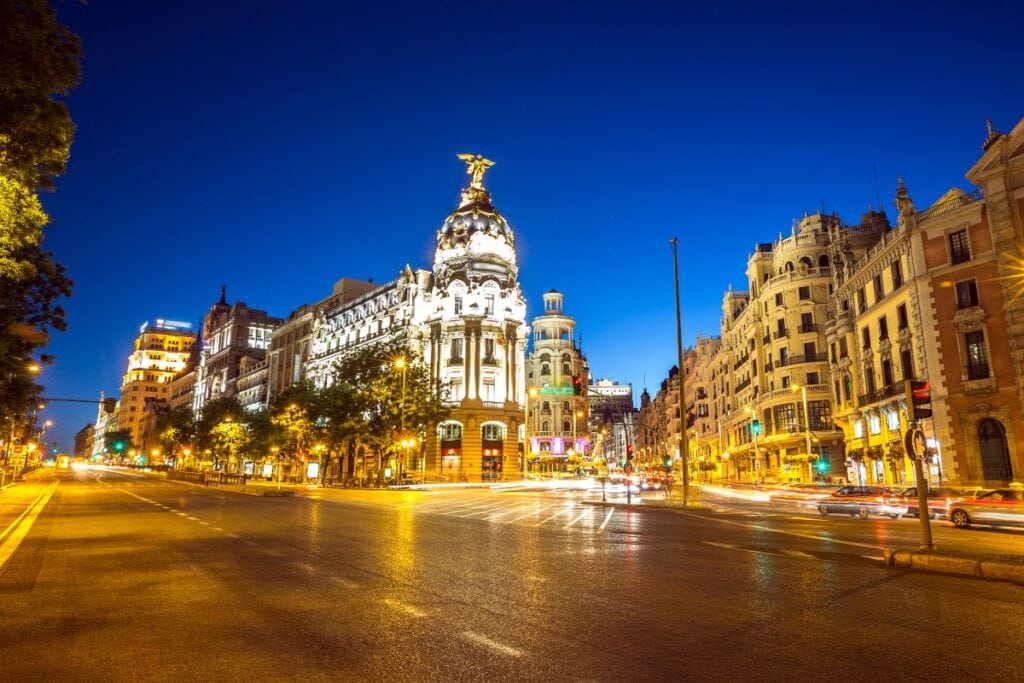 Gran Via in Madrid lit up at night with cars and pedestrians.