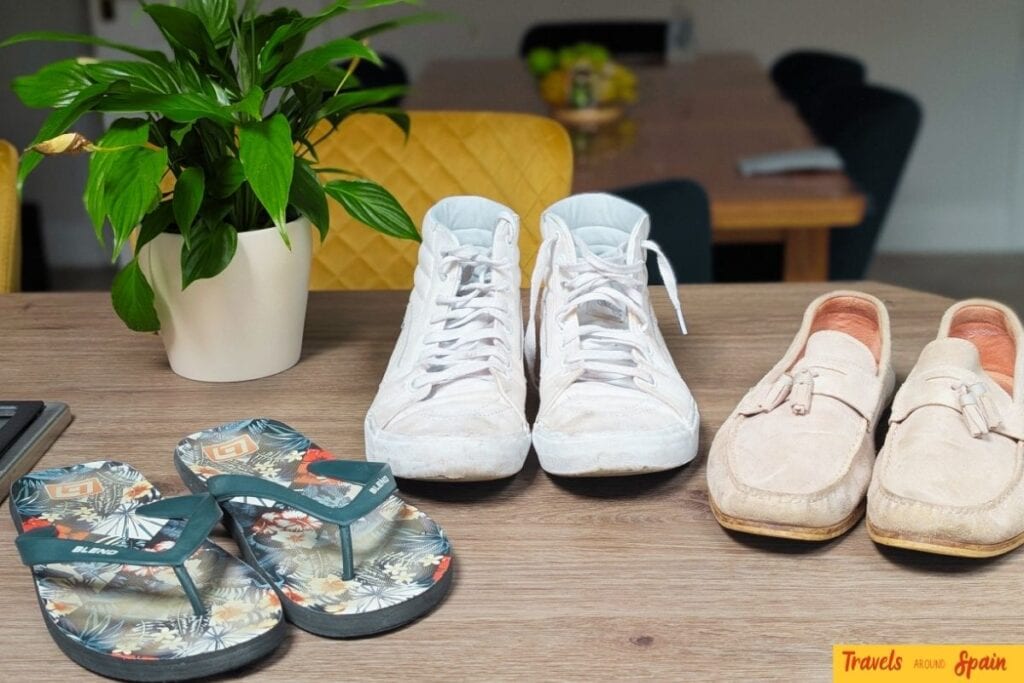 Three pairs of shoes for what to pack for Gran Canaria in June - colorful flip-flops, white trainers, and beige loafers arranged on wooden table
