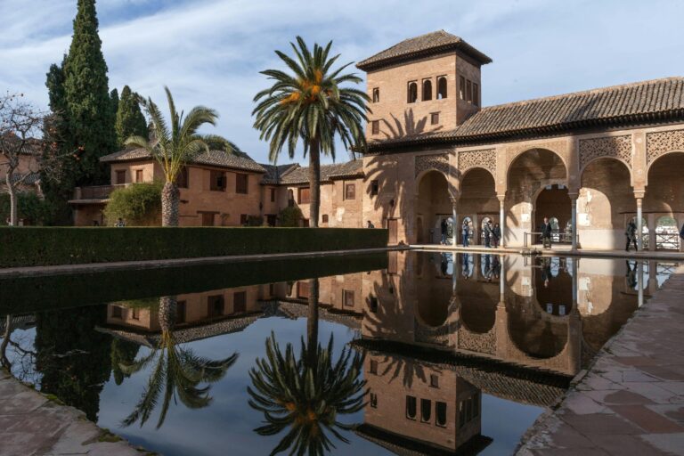 View of the Generalife palace and gardens in Granada, Spain, with a reflecting pool in the foreground, showcasing a must-see attraction when deciding where to stay in Granada, Spain.