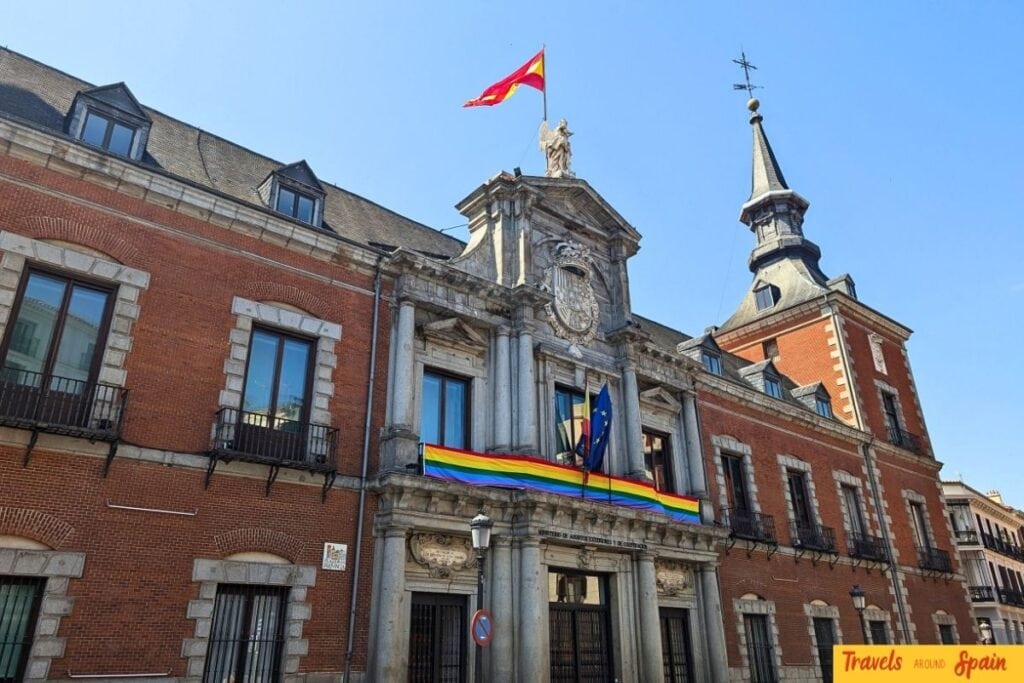 Spanish government building in Madrid with rainbow Pride flag on facade alongside national flags