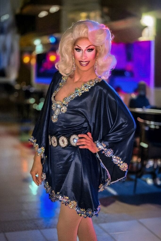 Miss Foguen drag queen in elegant black satin dress with blonde vintage curls at Sparkles Bar Maspalomas