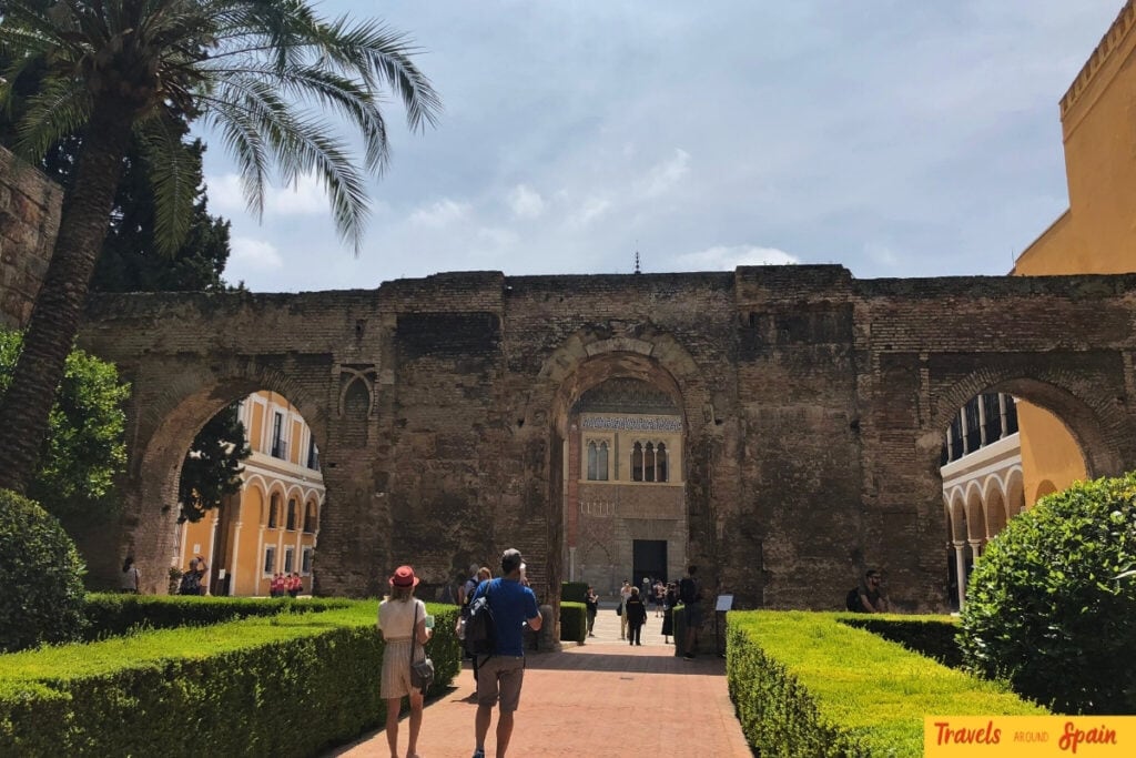 Lush green gardens at Real Alcázar with palm trees and tourists enjoying pleasant weather