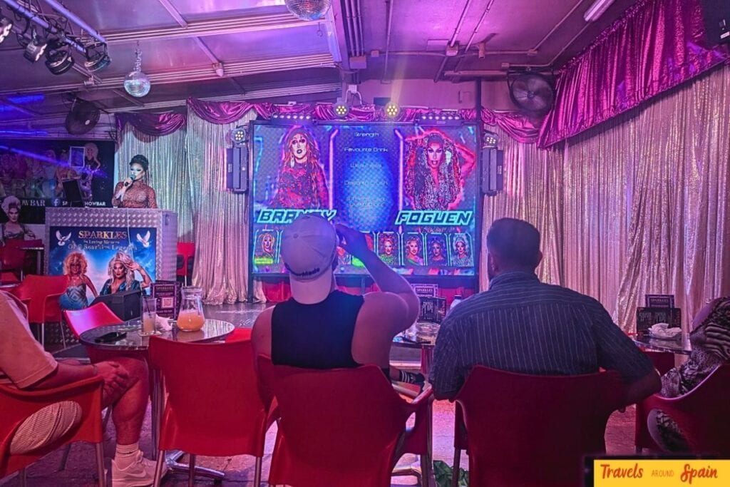 Live drag show at Sparkles Bar Maspalomas with LED screen displaying performer profiles and audience watching.