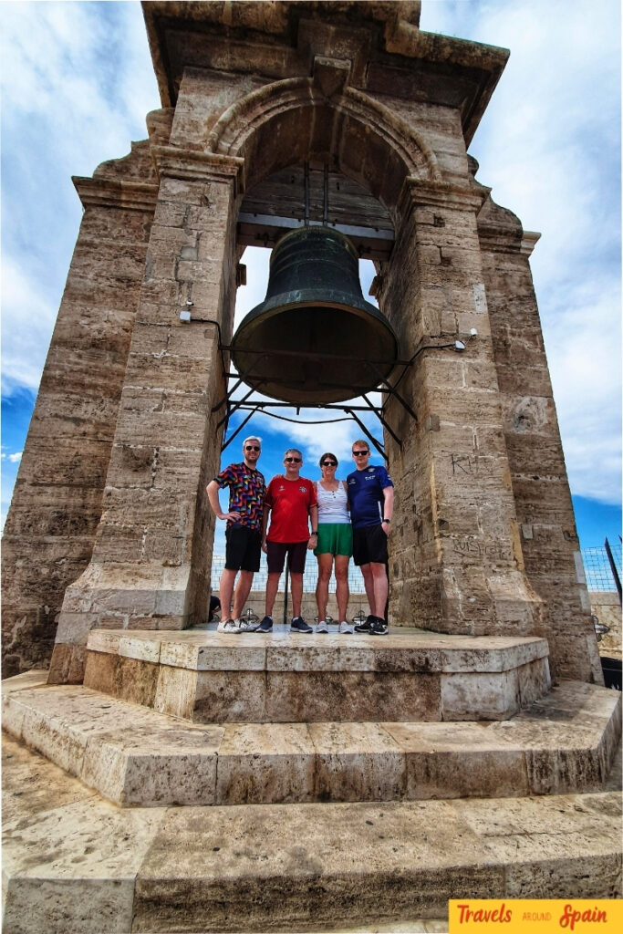 Family of four standing inside the medieval Miguelete Tower bell chamber with large bronze bell visible