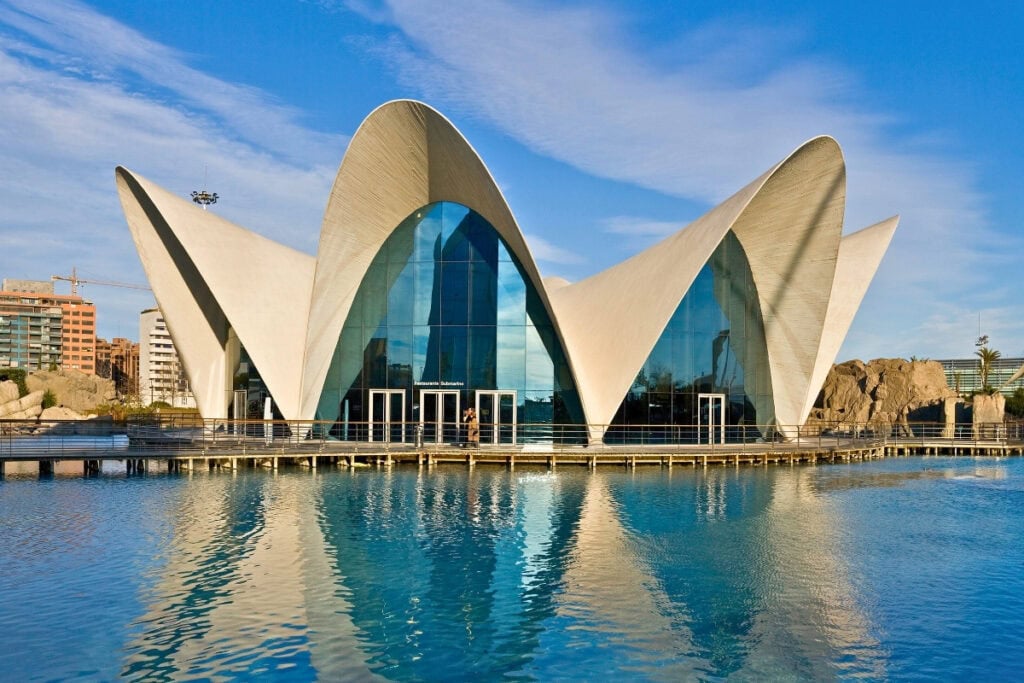 Modern curved white architecture of the Oceanogràfic aquarium reflected in surrounding blue water pools in Valencia
