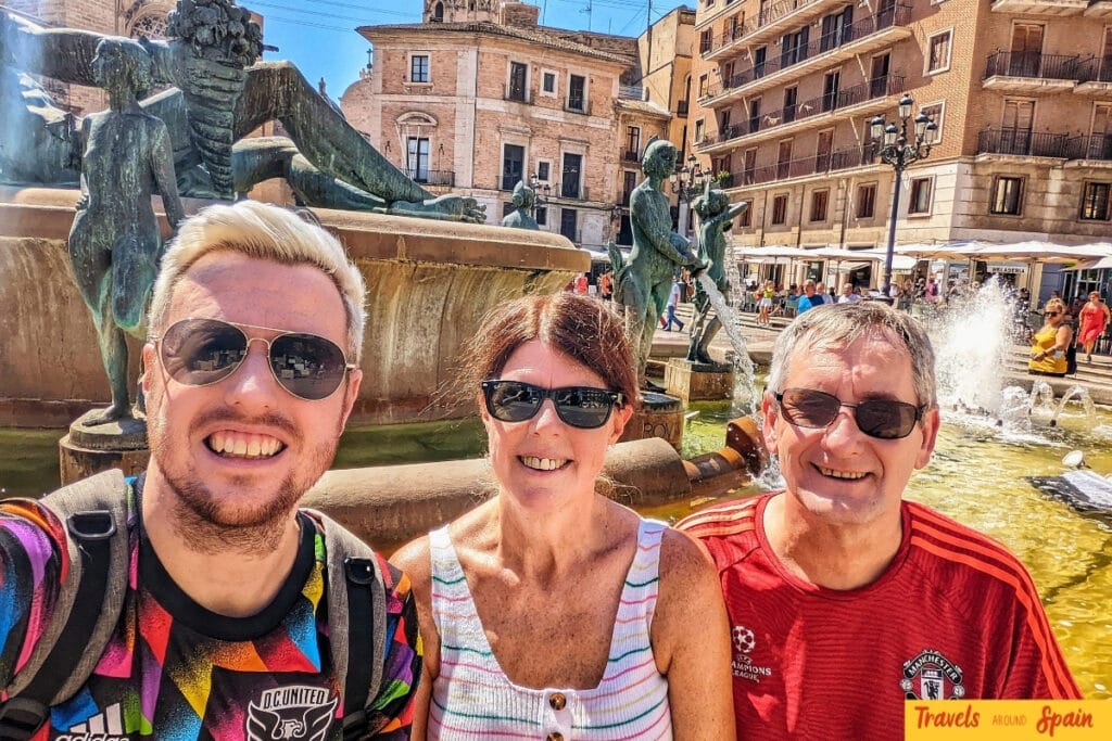 Three people taking a selfie at the baroque Fountain of Turia in Plaza de la Virgen, Valencia's most beautiful square