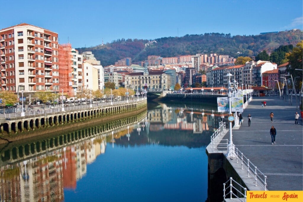 Nervión River with autumn hillside and historic buildings in Bilbao.