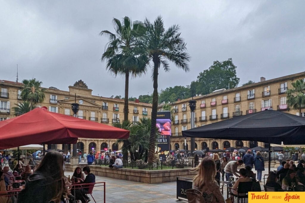 People sitting at café tables under umbrellas on a cloudy day in Bilbao Spain