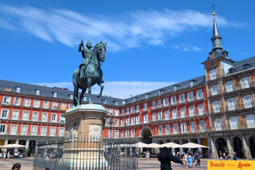 Plaza Mayor Madrid in September sunshine with statue and people walking in the square