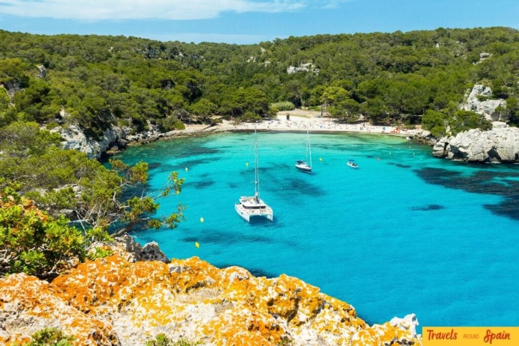 Turquoise cala beach in Menorca with boats and pine trees