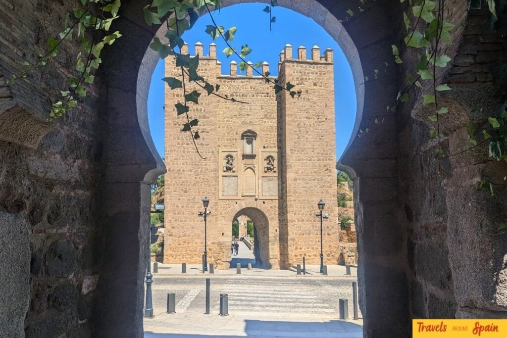Historic gate in Toledo framed by stone archway on a sunny summer day.